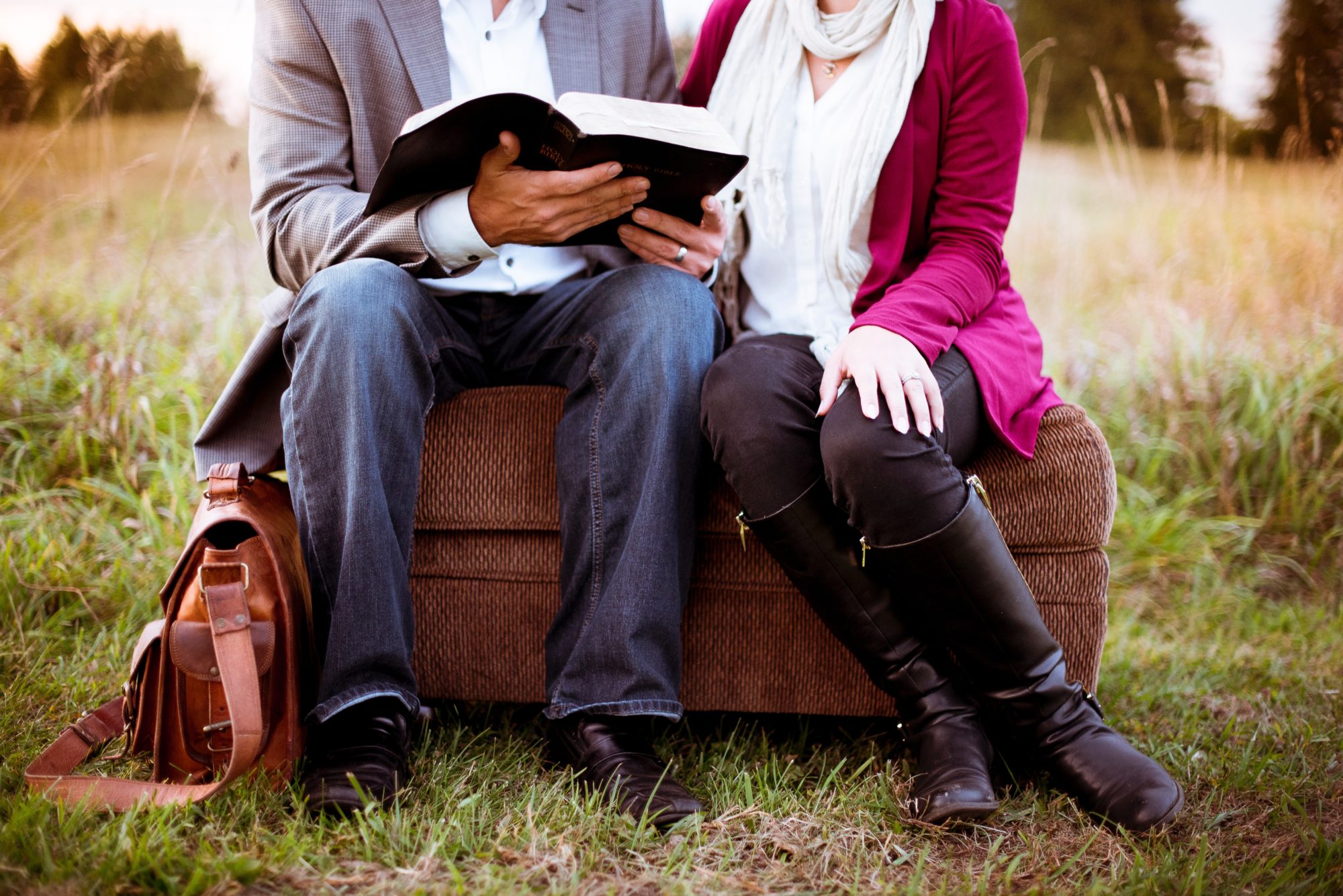 Two people sitting on a stool reading a book outside