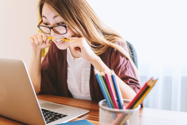 Woman looking frustrated and biting pencil looking at laptop