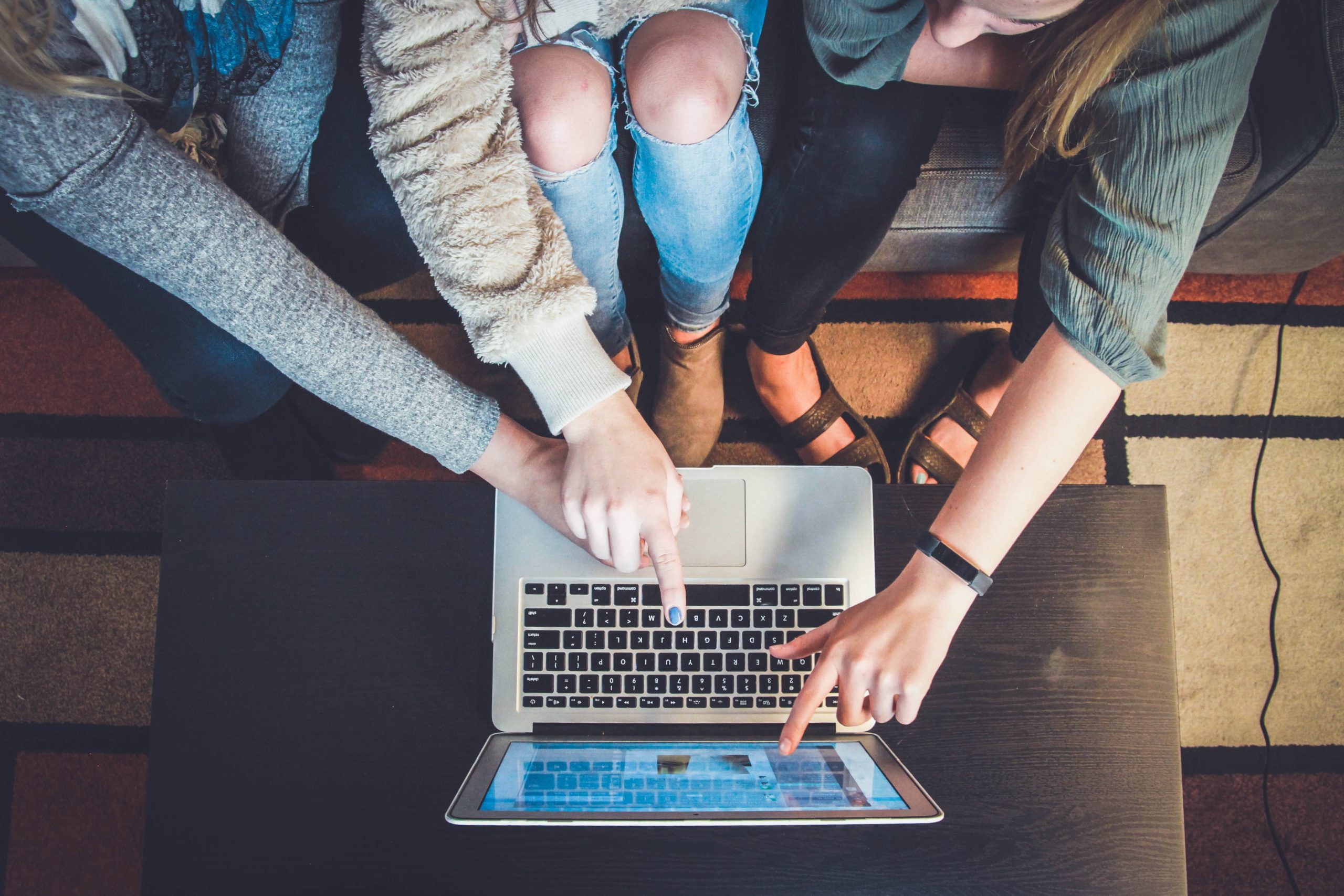 3 people leaning over table and pointing at laptop screen