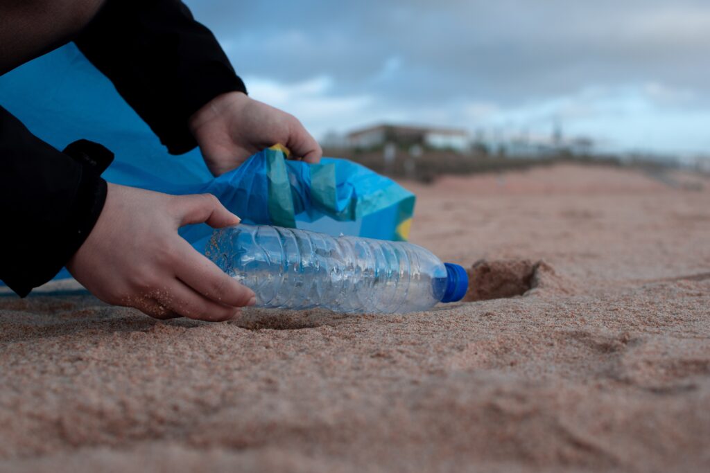 Person picking up plastic bottle from the beach to put in rubbish bag