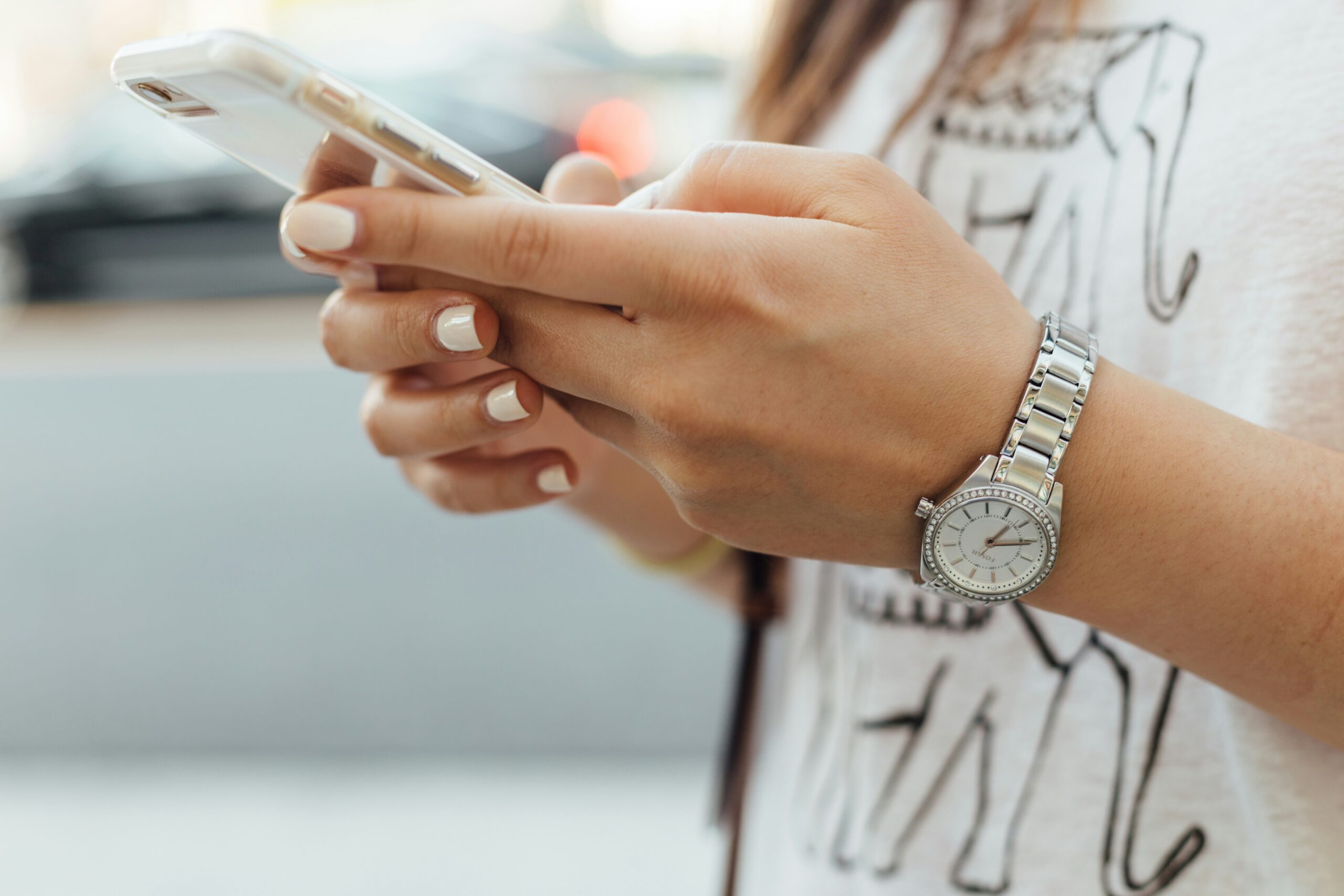 Hands of young woman with white nail varnish holding a smart phone.