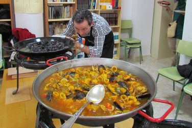 2 large dishes of paella, with the chef leaning over one to add the final touches.